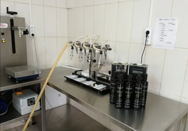 Masa de îmbuteliere Sirreon: rezervor de inox, mașină de umplut și sticle negre de ulei aliniate